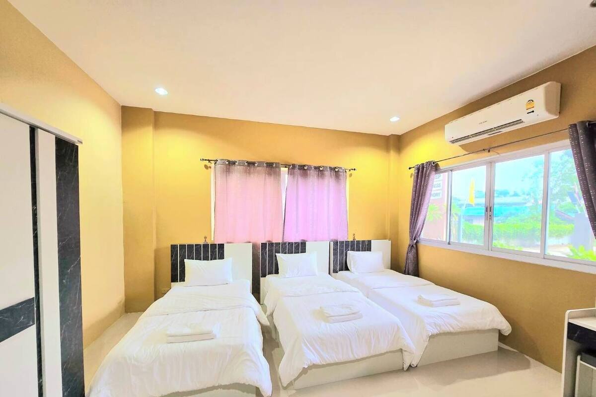 A hotel room with two beds, a window with curtains, an air conditioning unit, and a view of greenery outside.