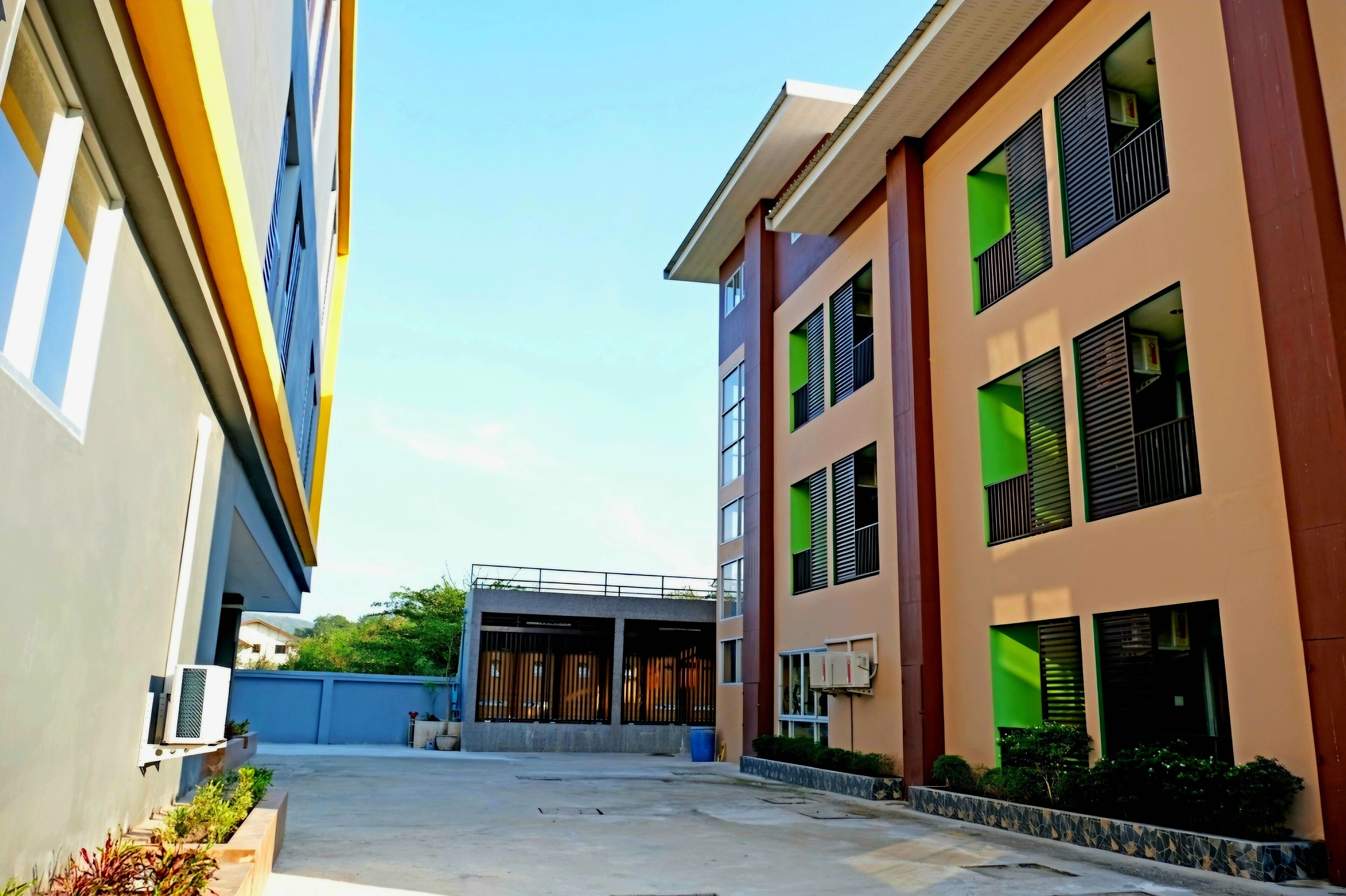 A modern building with multiple floors, large windows with green accents, and a covered entrance area.