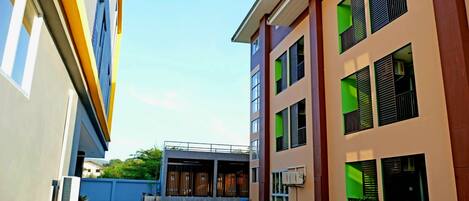 A modern building with multiple floors, large windows with green accents, and a covered entrance area.