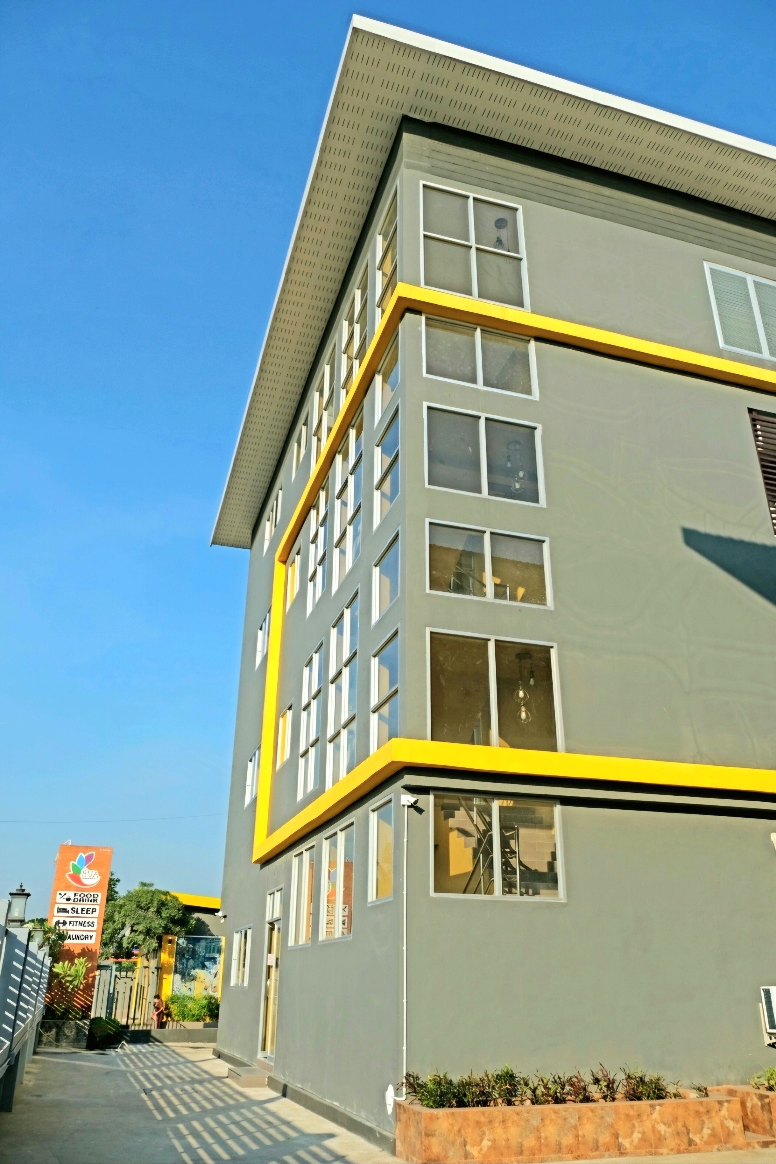 Un bâtiment moderne à la façade grise et aux ornements jaunes, doté de nombreuses fenêtres et d’une entrée bien visible.