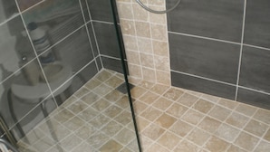 Un espace douche doté d’une porte en verre, de murs carrelés et d’un pommeau de douche.