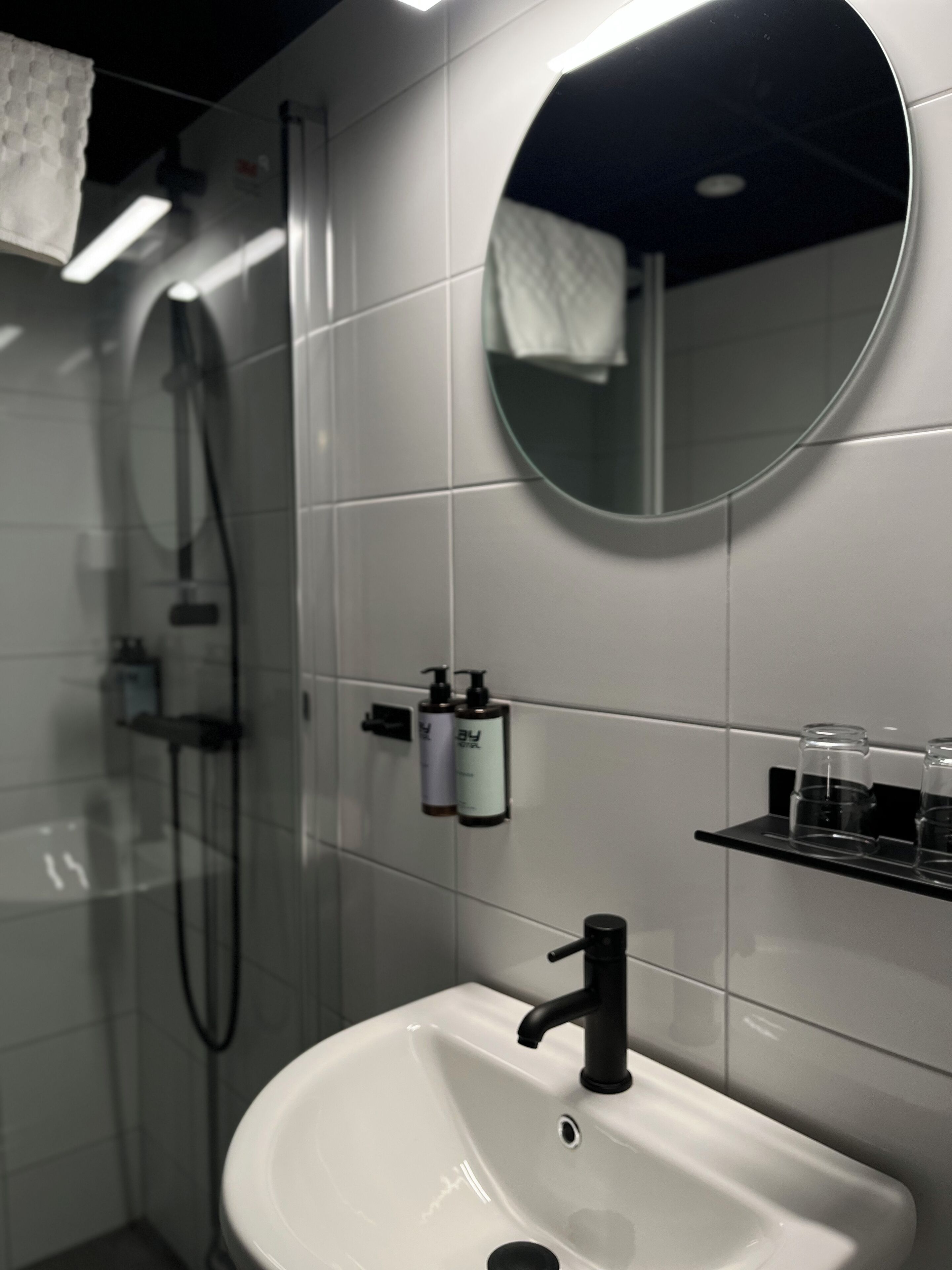 Une salle de bain moderne avec un lavabo blanc, un miroir rond et une cabine de douche en verre.