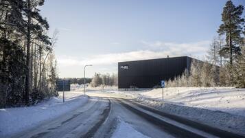 Una carretera cubierta de nieve que conduce a un gran edificio industrial con un letrero que dice 'PLAY'.