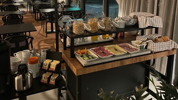 A modern dining area with a buffet setup, including various food items and a hanging plant arrangement. - Playhotel (Mjolby)