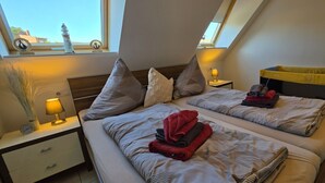 A bedroom with two beds, a skylight, a nightstand with a lamp, and a view of the outside. - Strandkrabbe: Your vacation by the sea! (Borkum)