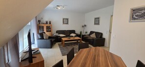 Un salon comprenant un ensemble de canapés, une table basse et un téléviseur. On y trouve également un meuble avec des portes en verre et une plante.