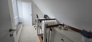 Eine Treppe mit weißer Handläufung, ein Schreibtisch mit Stuhl und ein kleiner Topf mit Pflanze auf der Zwischenebene.