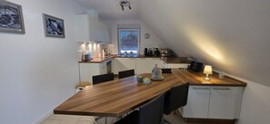 A compact kitchen with a wooden countertop, white cabinets, a dining table with chairs, and a window with blinds. - Strandkrabbe: Your vacation by the sea! (Borkum)