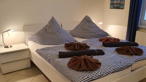 A neatly made bed with striped bedding and pillows, a bedside lamp, and a small bedside table. - Ferienwohnung Borkumgarten (Borkum)