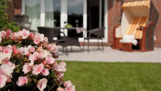 A patio area with a table and chairs, a brick wall, and a large window. - Ferienwohnung Borkumgarten (Borkum)