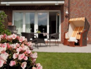 A patio area with a table and chairs, a brick wall, and a large window. - Ferienwohnung Borkumgarten (Borkum)