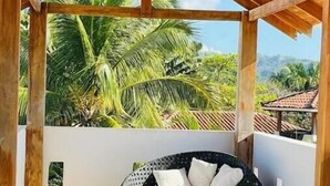 A covered outdoor seating area with a black woven chair and cushions, surrounded by palm trees and a clear view of the sky. - Hermosa palms beach house (Playa Hermosa)