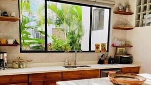 A kitchen with wooden cabinets, a marble countertop, a window with a view of greenery, and a small island with stools. - Hermosa palms beach house (Playa Hermosa)