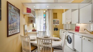 A compact kitchen with white cabinets, a washing machine, and a dining area with a table set for two. - La Maison in Albaro by Wonderful Italy (Genoa)