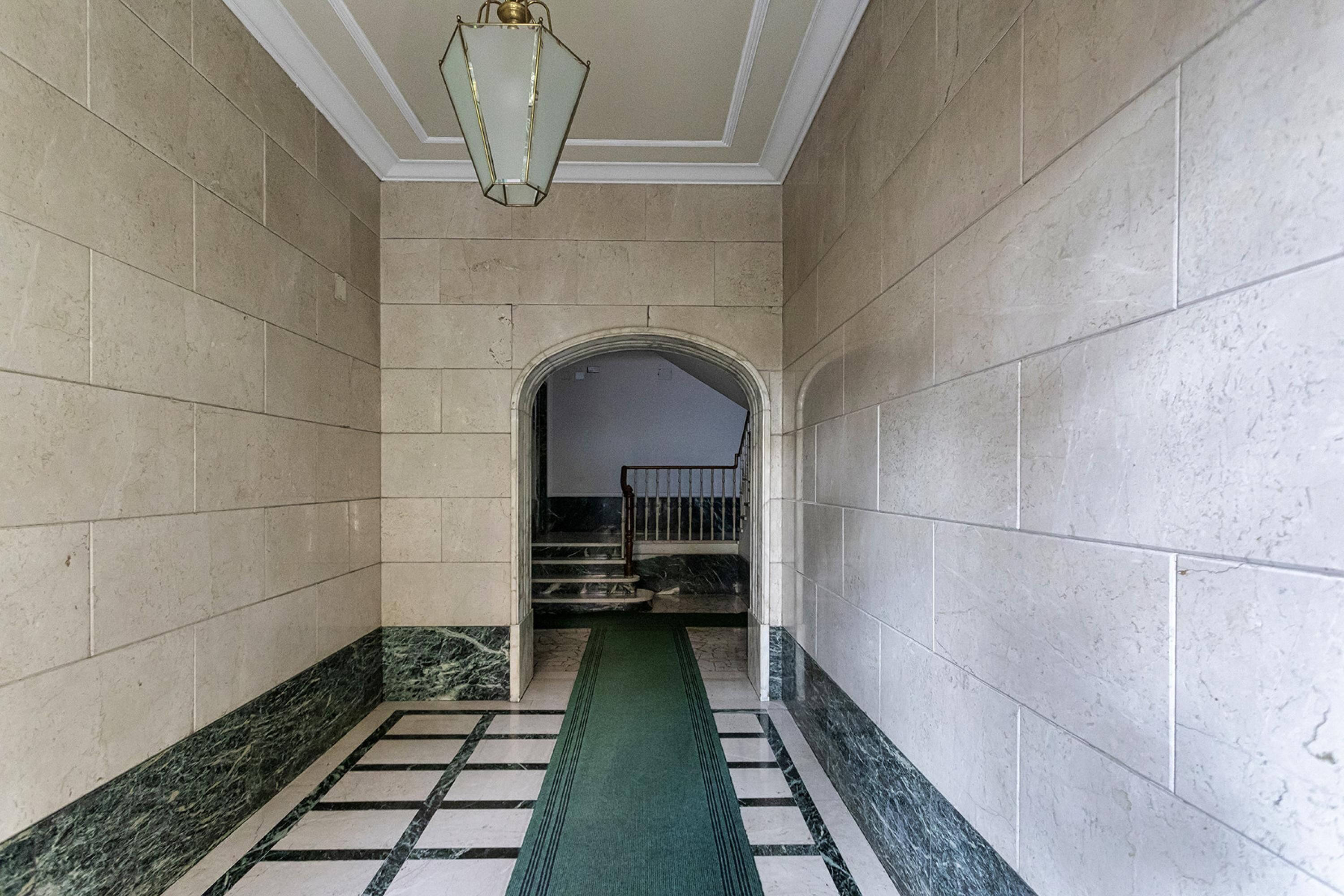 Un pasillo con paredes de mármol, alfombra verde y una escalera que sube a un nivel superior.