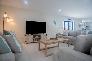 En moderne stue med et fladskærms TV, grå sofaer, et træ sofabord og et skab med legetøj.