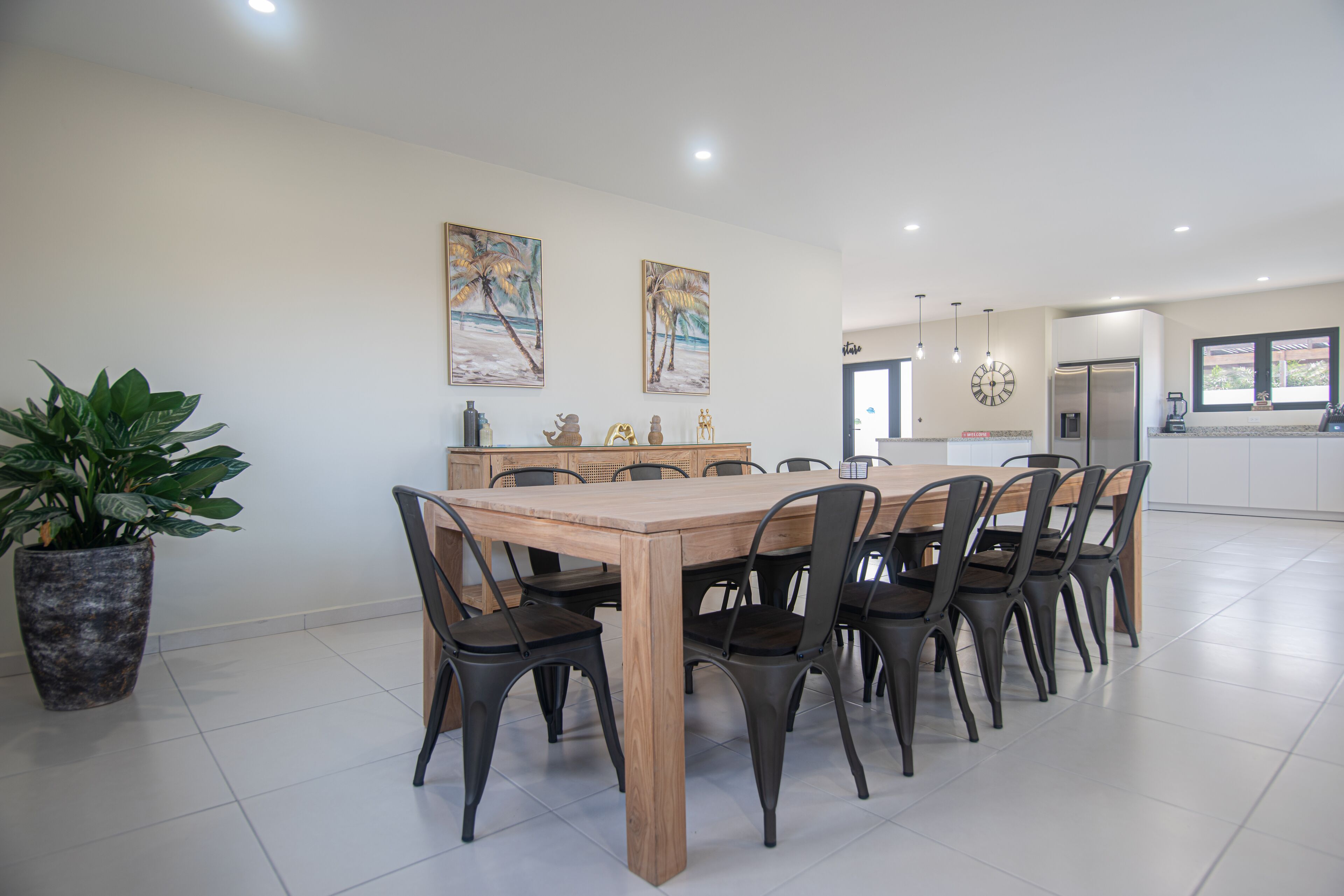 Une cuisine moderne dotée d’un grand îlot central, d’un coin repas avec une table et des chaises en bois, et d’une plante en pot.