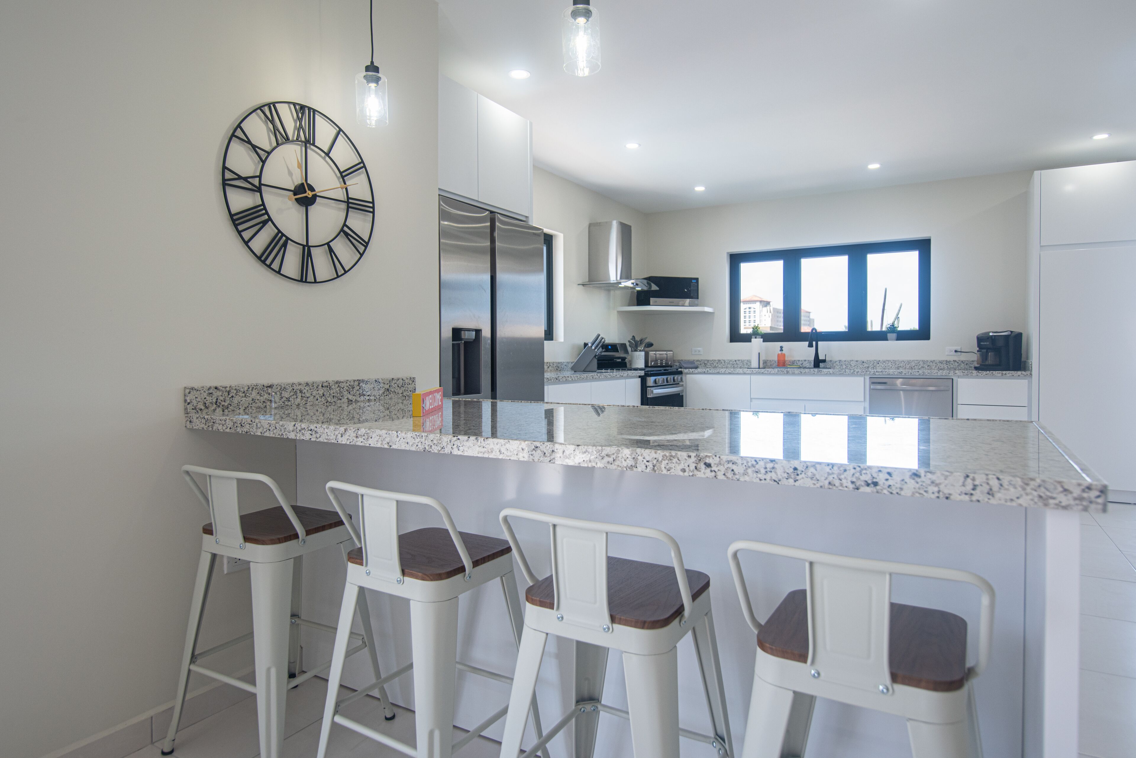 Une cuisine moderne dotée d’un grand îlot central, de tabourets de bar, d’appareils électroménagers en acier inoxydable et d’une horloge murale.