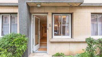Un bâtiment moderne avec une façade recouverte de carreaux, un numéro « 5 » bien visible sur la porte et un petit hall d’entrée avec une marche.