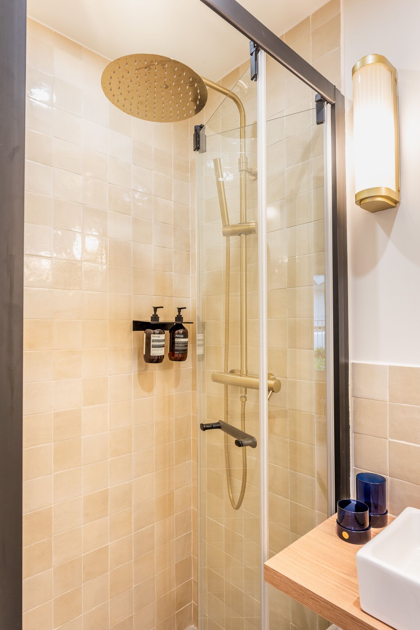 Een moderne douche met een regendouche, een glazen cabine en een houten plank met toiletartikelen.