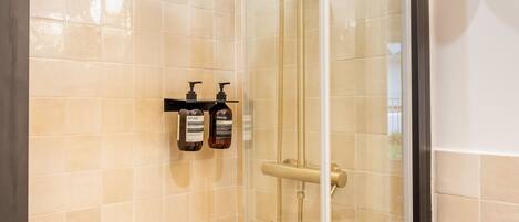 Een moderne douche met een regendouche, een glazen cabine en een houten plank met toiletartikelen.