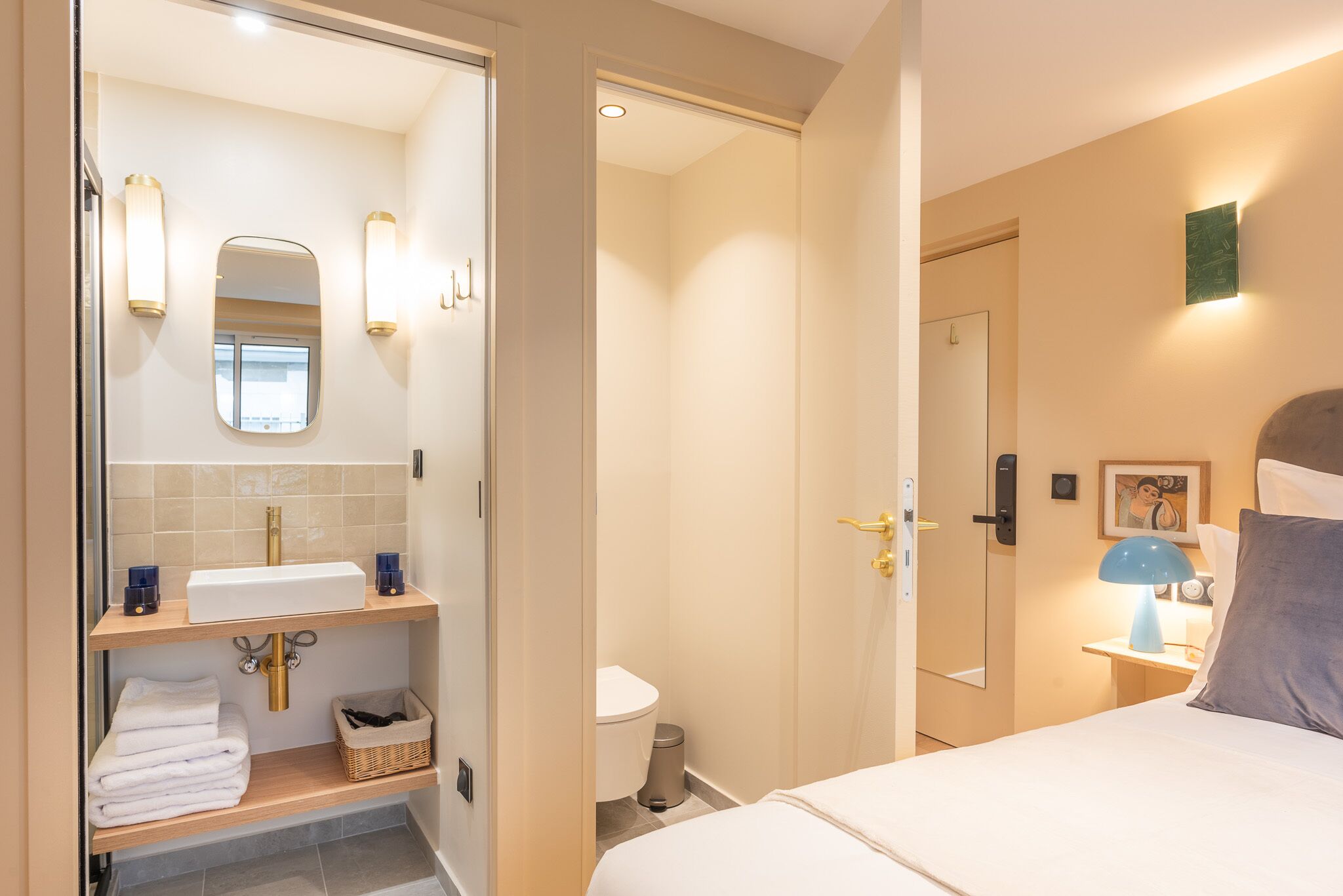 Et hotelværelse med badeværelse, seng, natbord og væglampe.