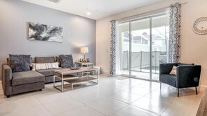 Ein modernes Wohnzimmer mit einem grauen Sofa, einem Couchtisch und einem schwarzen Sessel. Ein großes Fenster bietet Blick auf Häuser.