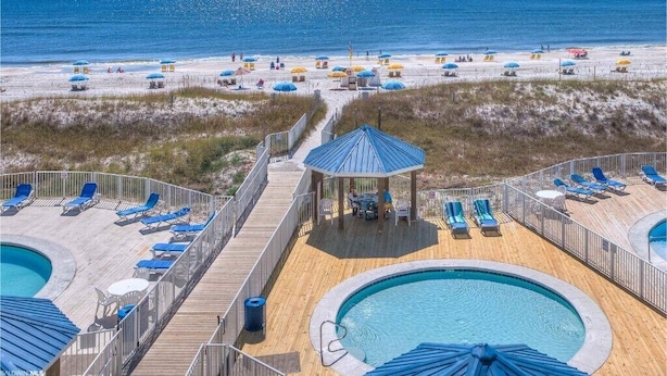 A pool area with lounge chairs and umbrellas, a wooden deck, and a view of the beach. - Sept 12-17 DISCOUNT! Updated Right on the beach! Umbrella,2chairs,2beach towels! (Orange Beach)