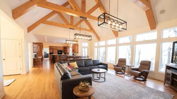 A spacious living room with a high ceiling, wooden beams, a dark-colored sofa set, and a fireplace. - Secluded Spa-cious Retreat -Beds for 8. Plus 3 foldaways extra (Minneapolis)