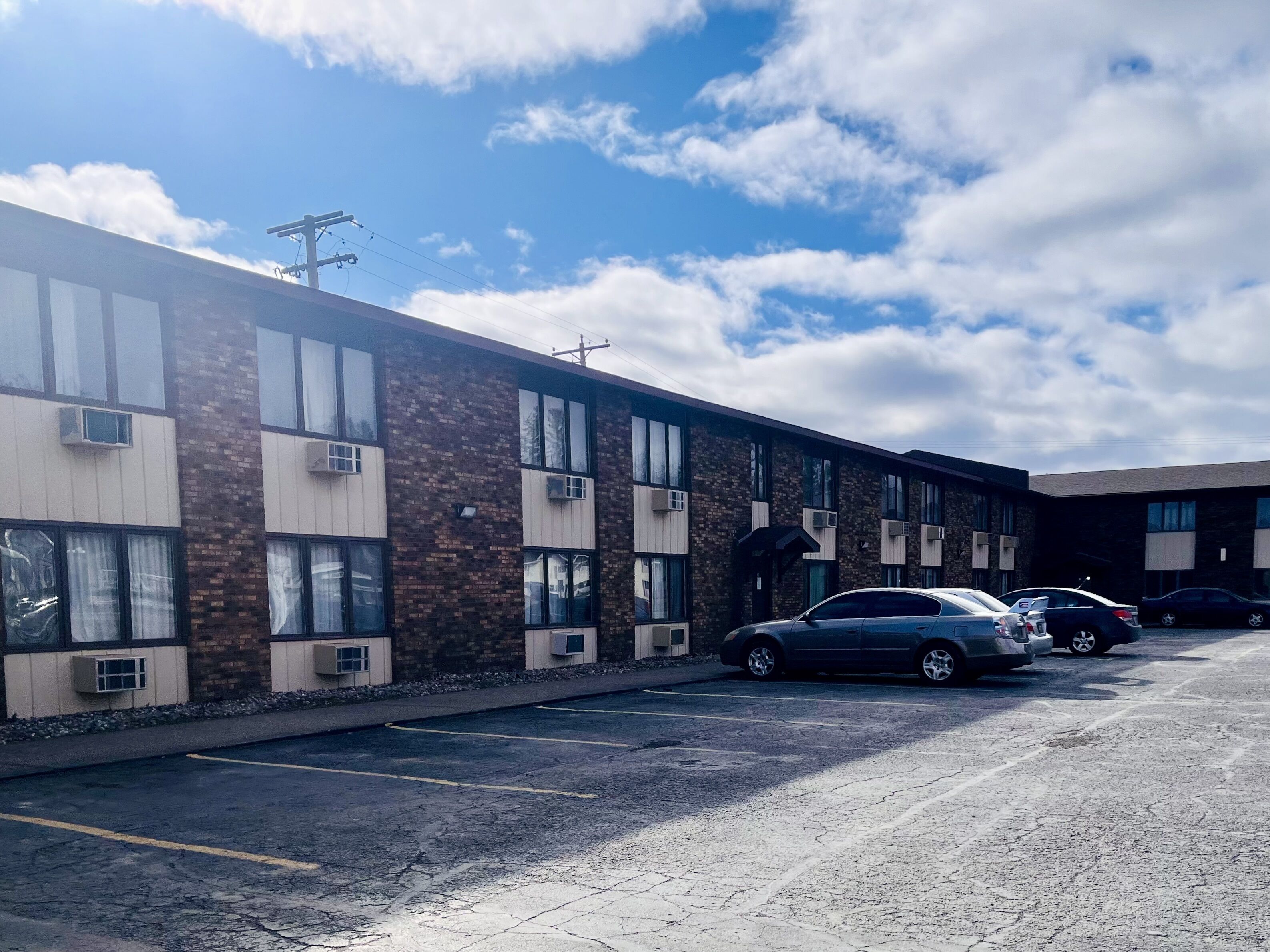 A multi-story building with a brick facade and large windows. There are several parked cars in the adjacent parking lot.