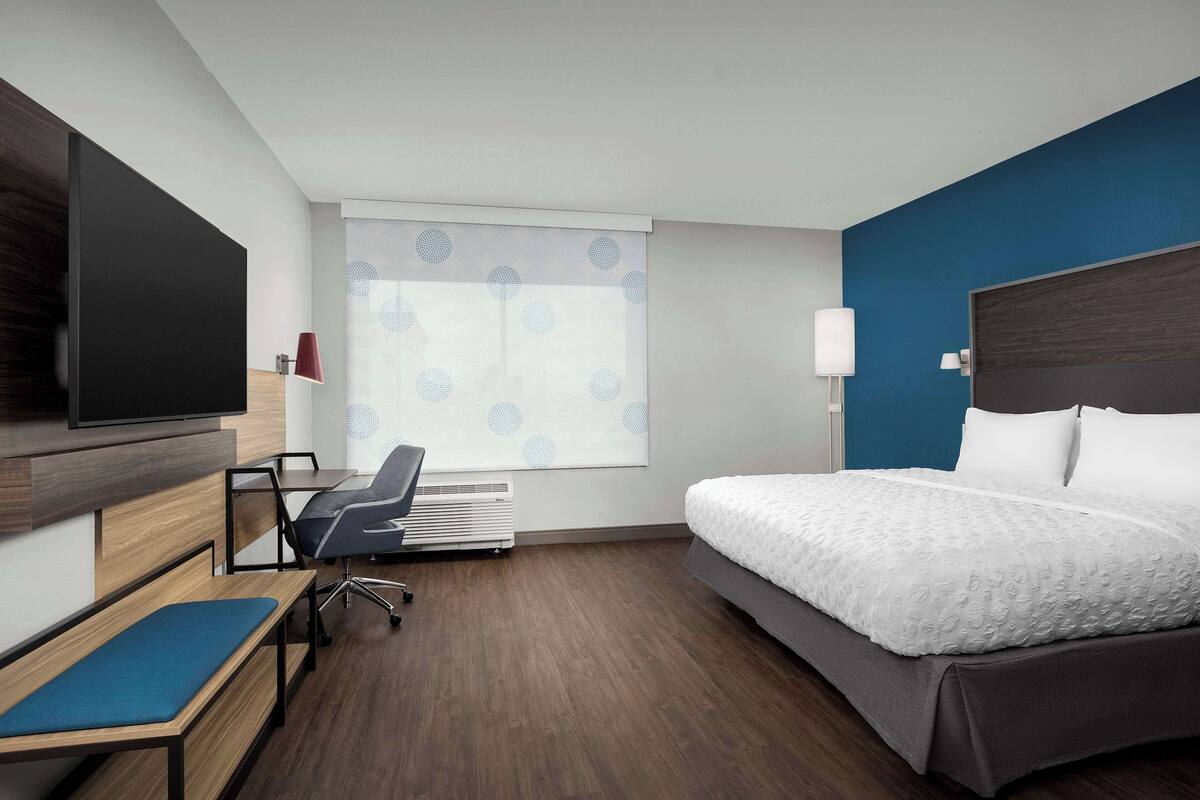 A hotel room with a bed, a desk, a chair, a TV, and a window with a view.