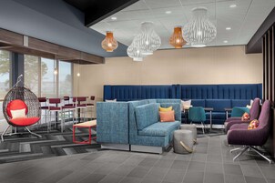 A modern lounge area with a blue sofa, red and purple chairs, and a hanging chair with a red cushion.