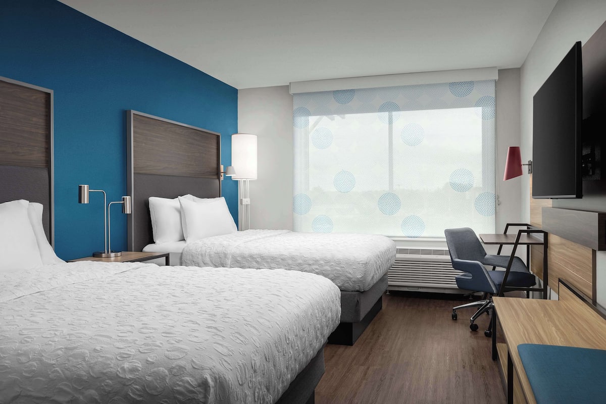 A hotel room with two beds, a desk, a chair, a TV, and a window with a view.