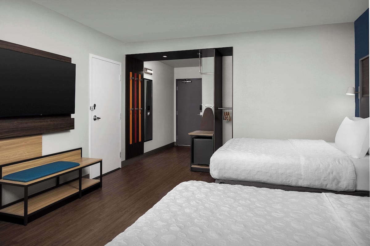 A modern hotel room with a large bed, a bench, a TV, and a wardrobe.