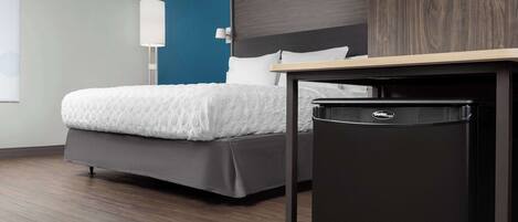 Una habitación de hotel moderna con una cama, un cubo de basura negro pequeño y una lámpara fijada a la pared.