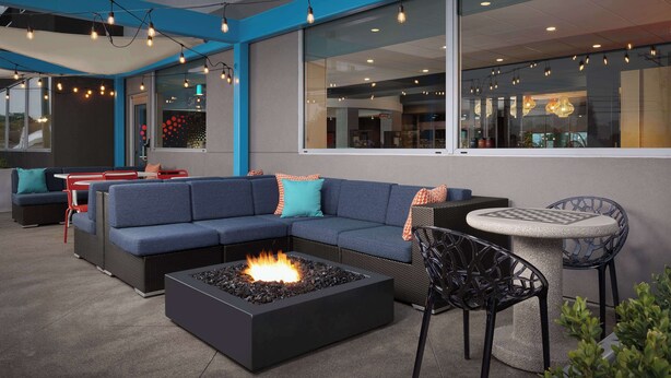 An outdoor seating area with a fire pit, blue sofas, and a round table. - Tru By Hilton Columbus East Broad (Columbus)
