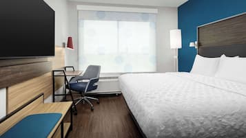 A hotel room with a bed, a desk, a chair, a TV, and a window with patterned curtains.