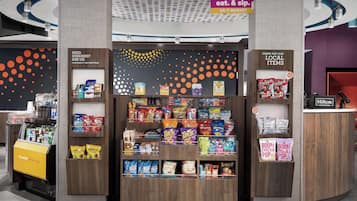 A snack kiosk with a variety of snacks and beverages, a front desk area, and a sign indicating 24/7 market availability.
