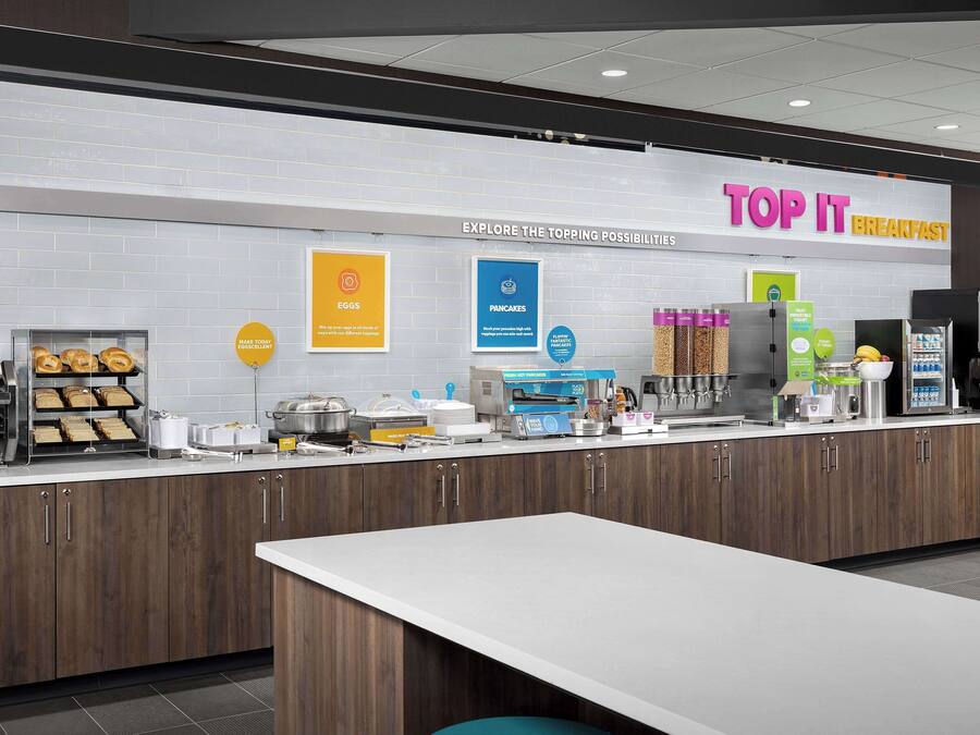 A breakfast area with a sign reading "TOP IT BREAKFAST" and various food options like eggs and pancakes.