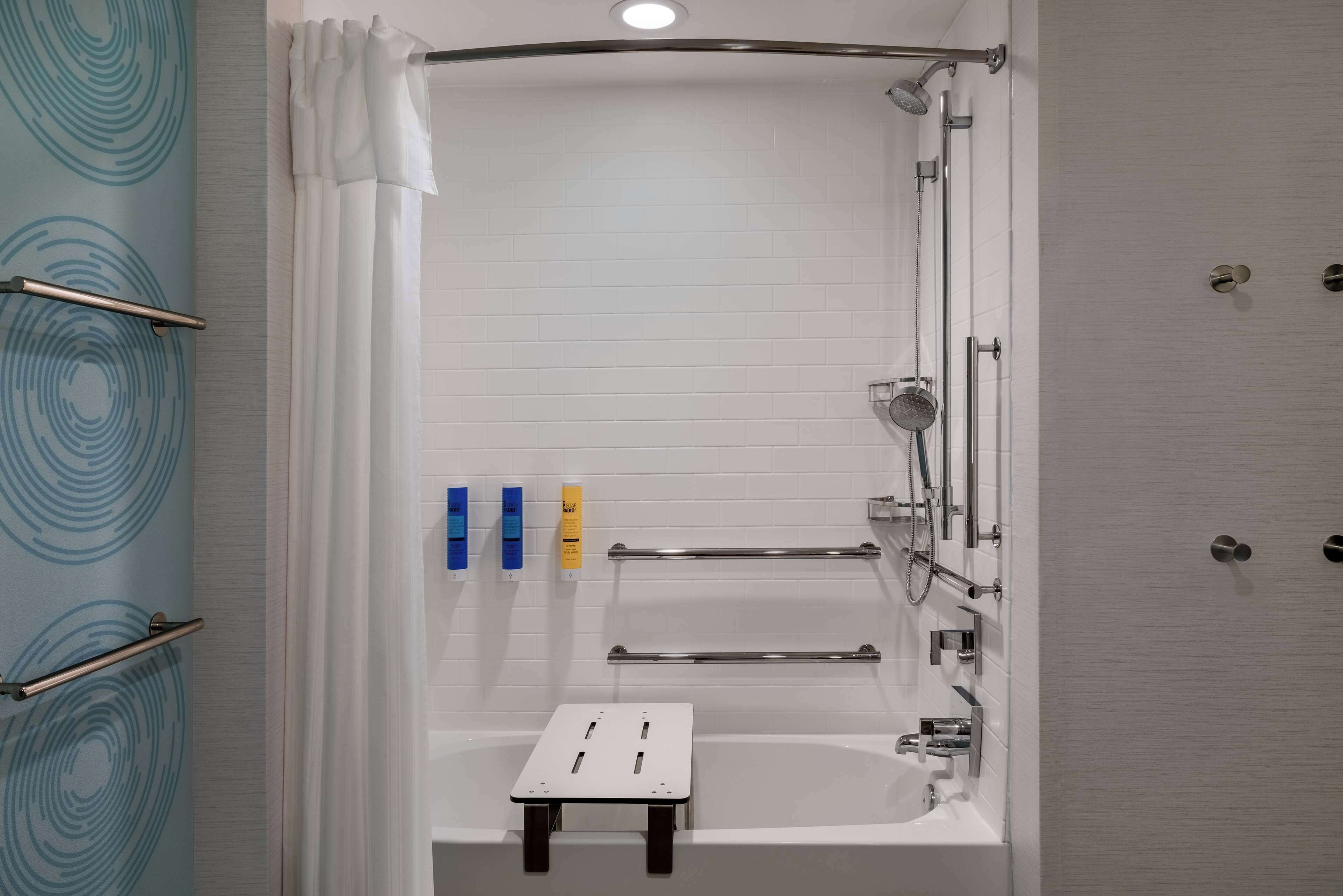 A modern bathroom with a shower, a small step stool, and handrails.