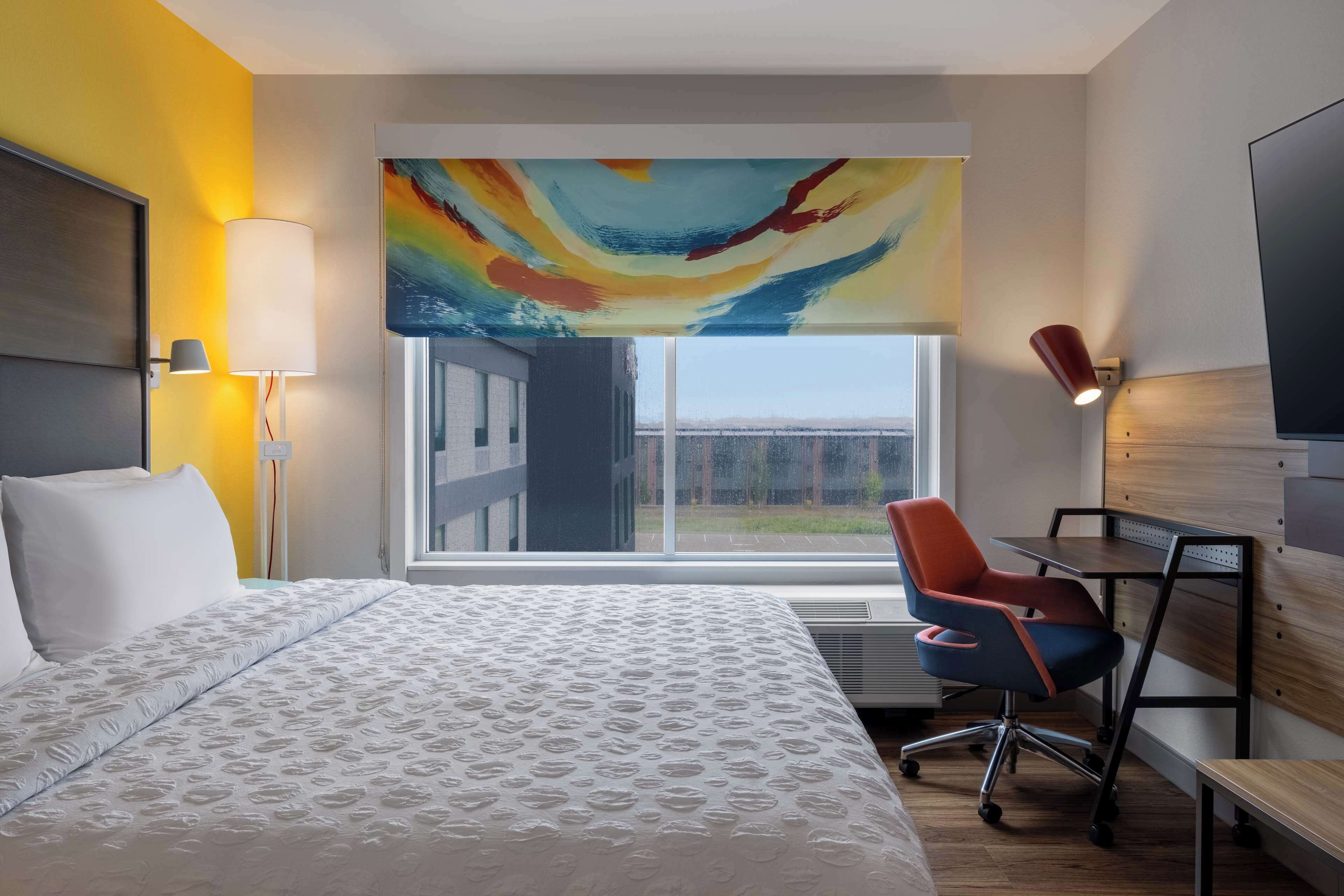 A hotel room with a bed, a desk, a chair, a TV, and a large window with a view.