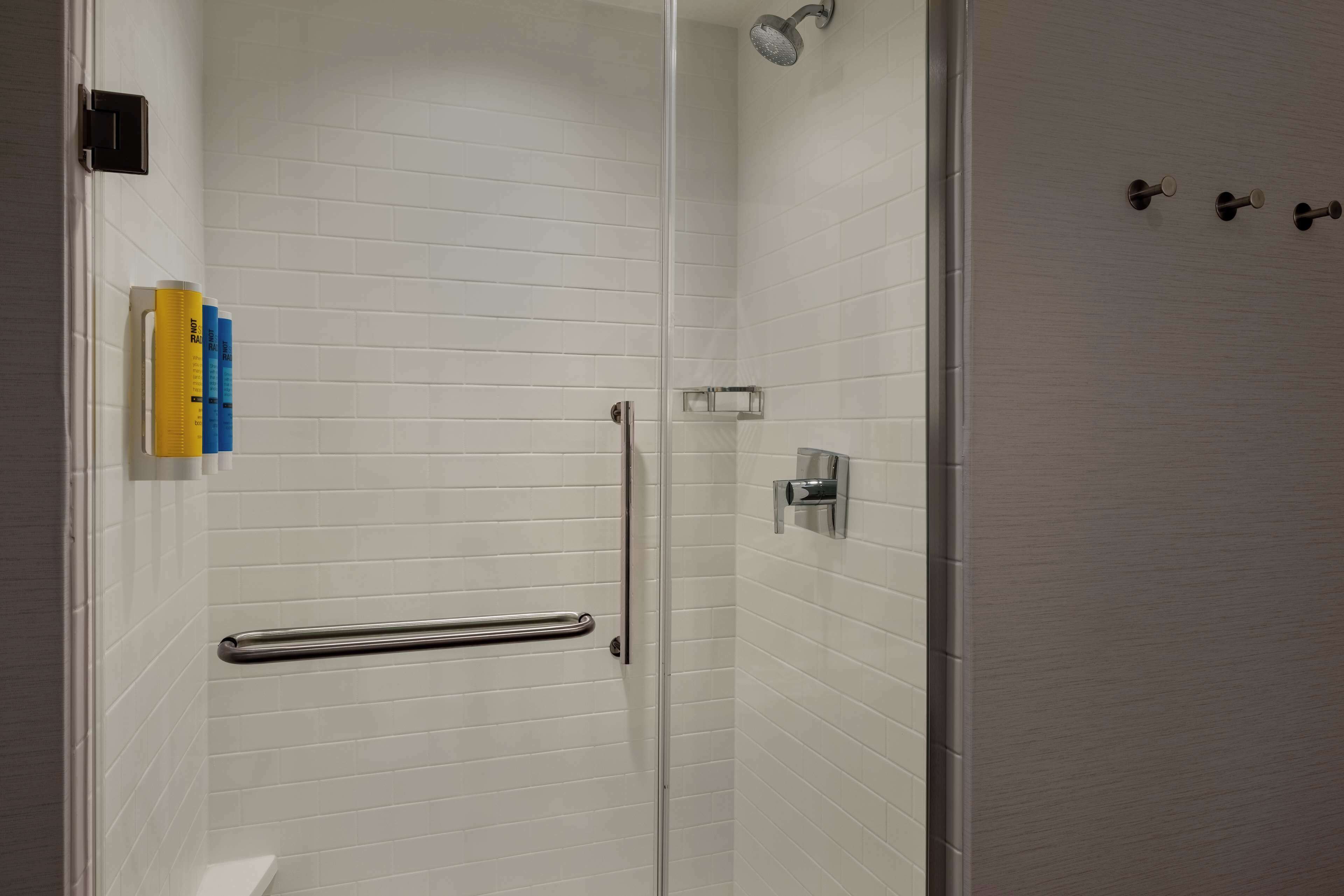 Une douche moderne dotée d’une porte en verre, d’une barre d’appui et d’un distributeur de serviettes fixé au mur.