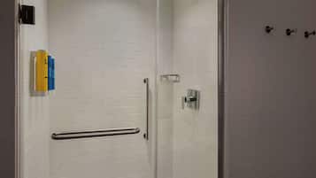 A modern shower with a glass door, a handrail, and a wall-mounted towel dispenser.