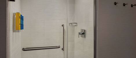 A modern shower with a glass door, a handrail, and a wall-mounted towel dispenser.