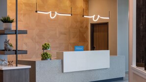 A hotel reception desk with a modern design, featuring a wooden wall pattern, a sign indicating it's a Hilton property, and a reception counter. - Tru By Hilton Ankeny (Ankeny)
