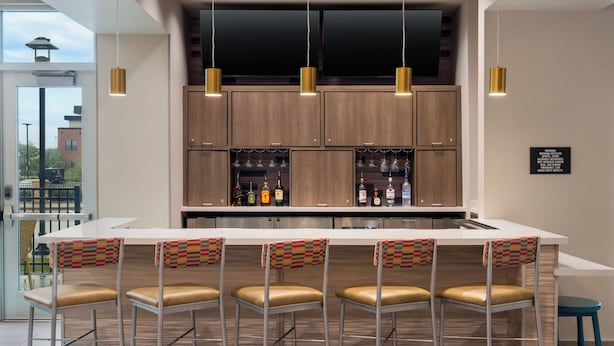 A modern kitchen with a bar area, wooden cabinets, and a large window. - Tru By Hilton Ankeny (Ankeny)