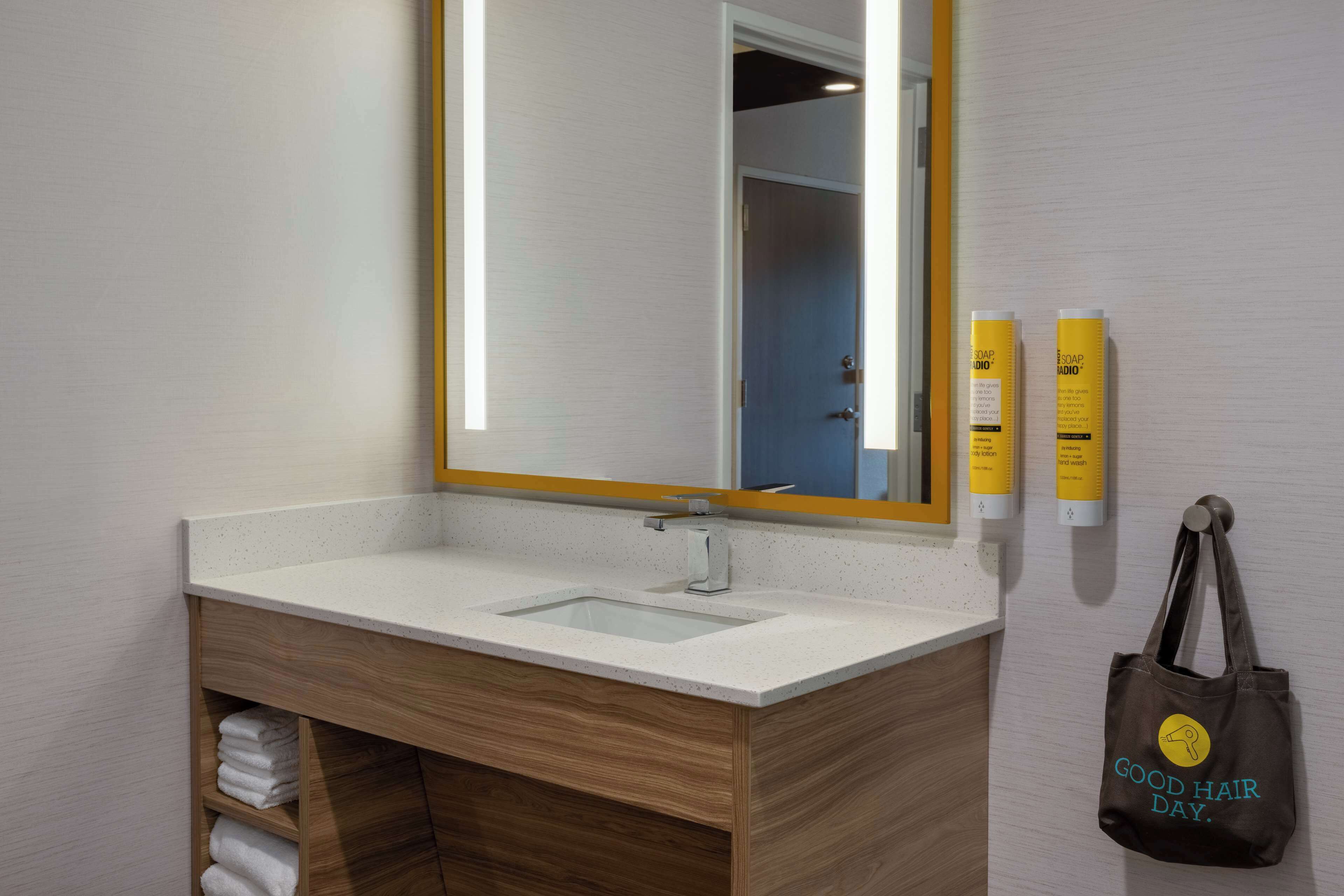 A bathroom with a wooden vanity, a sink, a mirror, and two soap dispensers.