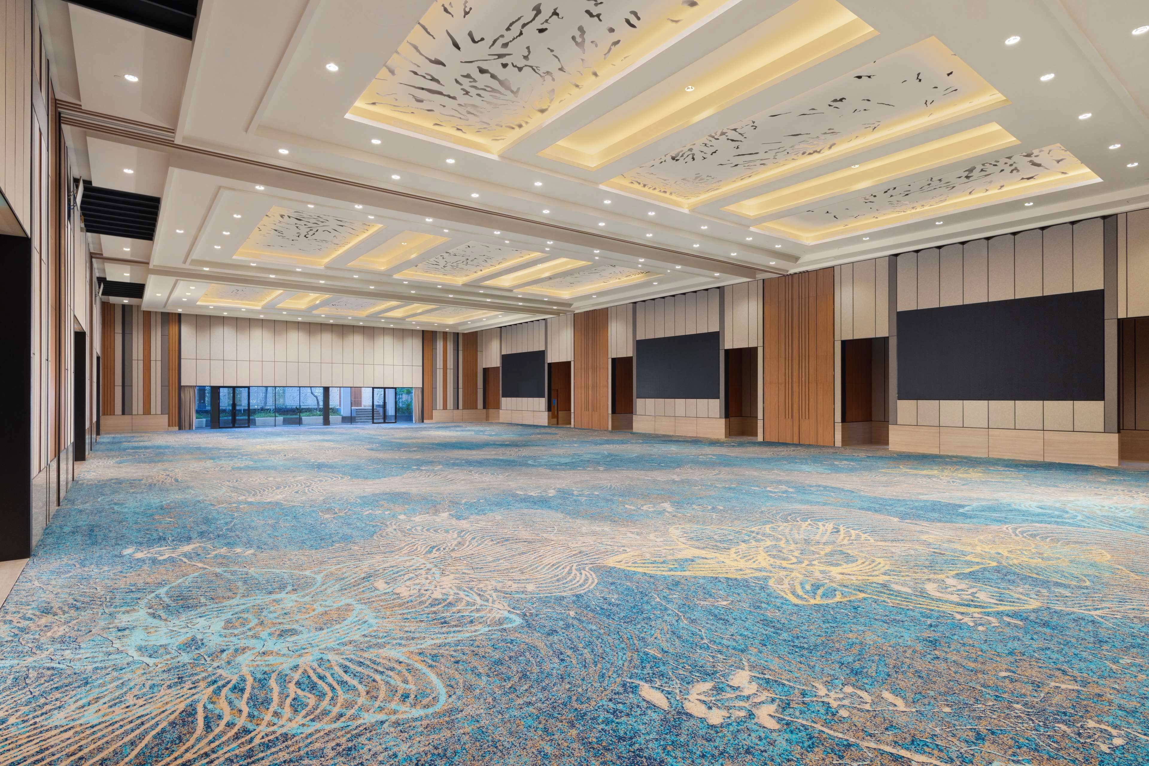 A spacious hotel lobby with a patterned carpet, recessed lighting, and a view of the outdoors.