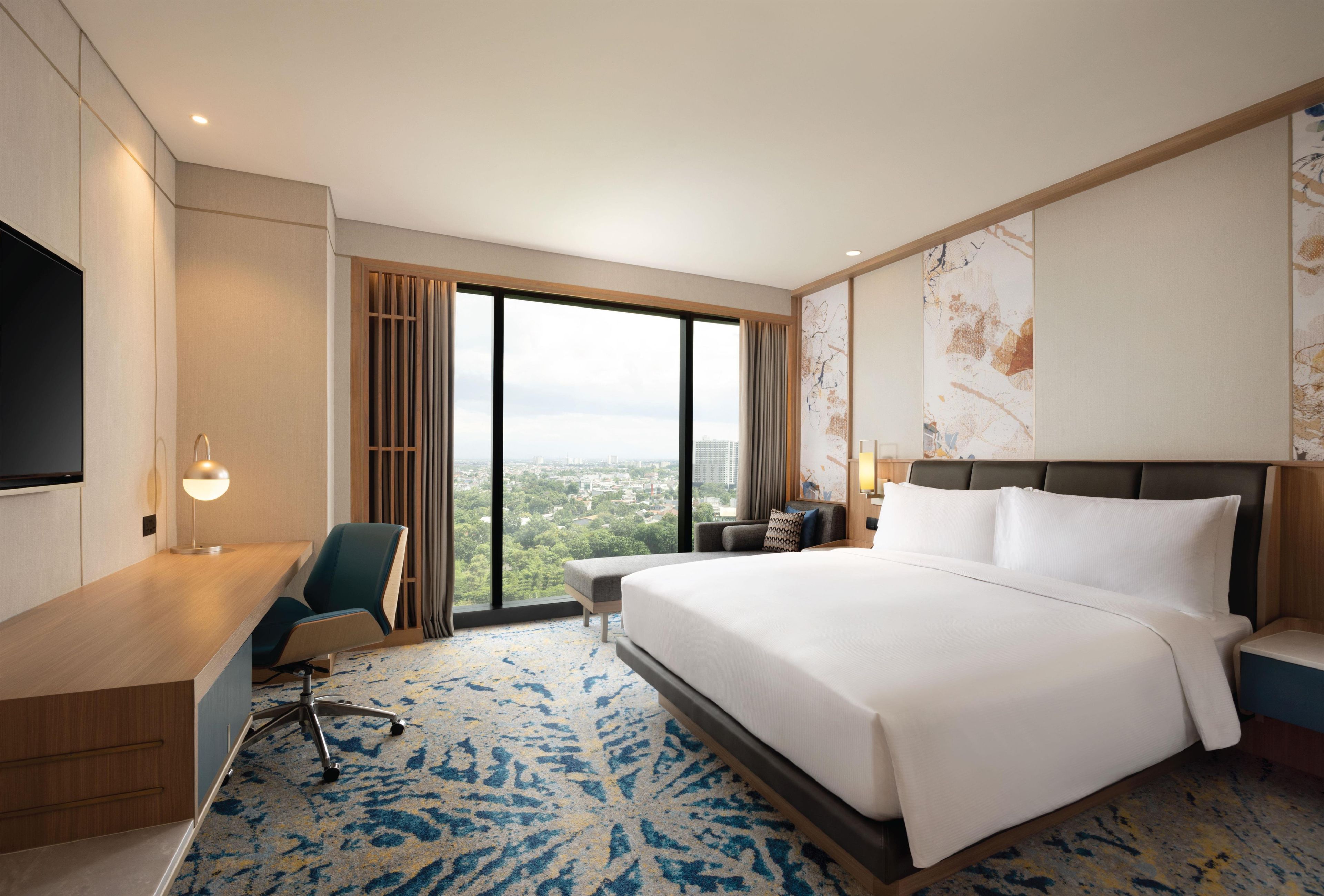 Une chambre d’hôtel avec un grand lit, un bureau, une chaise, une télévision et une vue sur la ville.