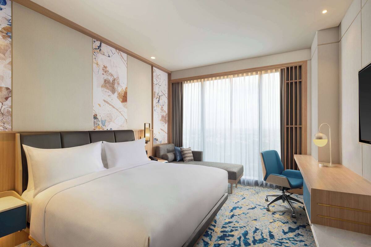 A hotel room with a large bed, a desk, a chair, and a TV.
